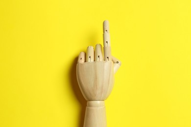 Photo of Wooden mannequin hand on yellow background, top view