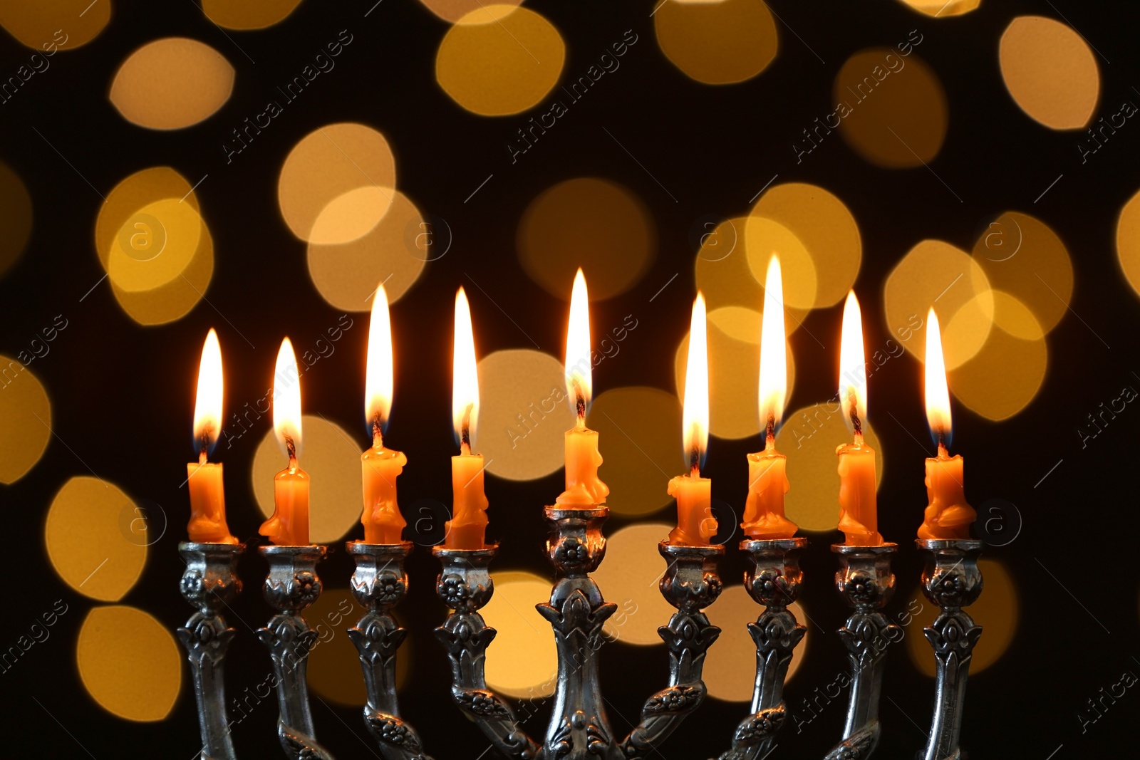 Photo of Silver menorah with burning candles against dark background and blurred festive lights. Hanukkah celebration