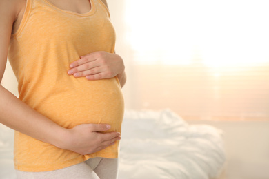 Photo of Young pregnant woman in bedroom, closeup. Space for text