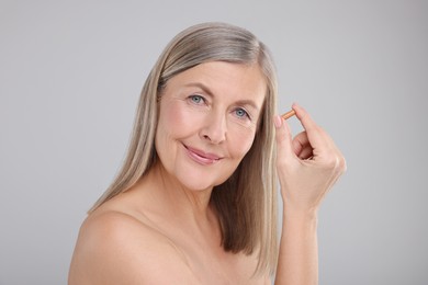 Photo of Beautiful woman with vitamin capsule on grey background