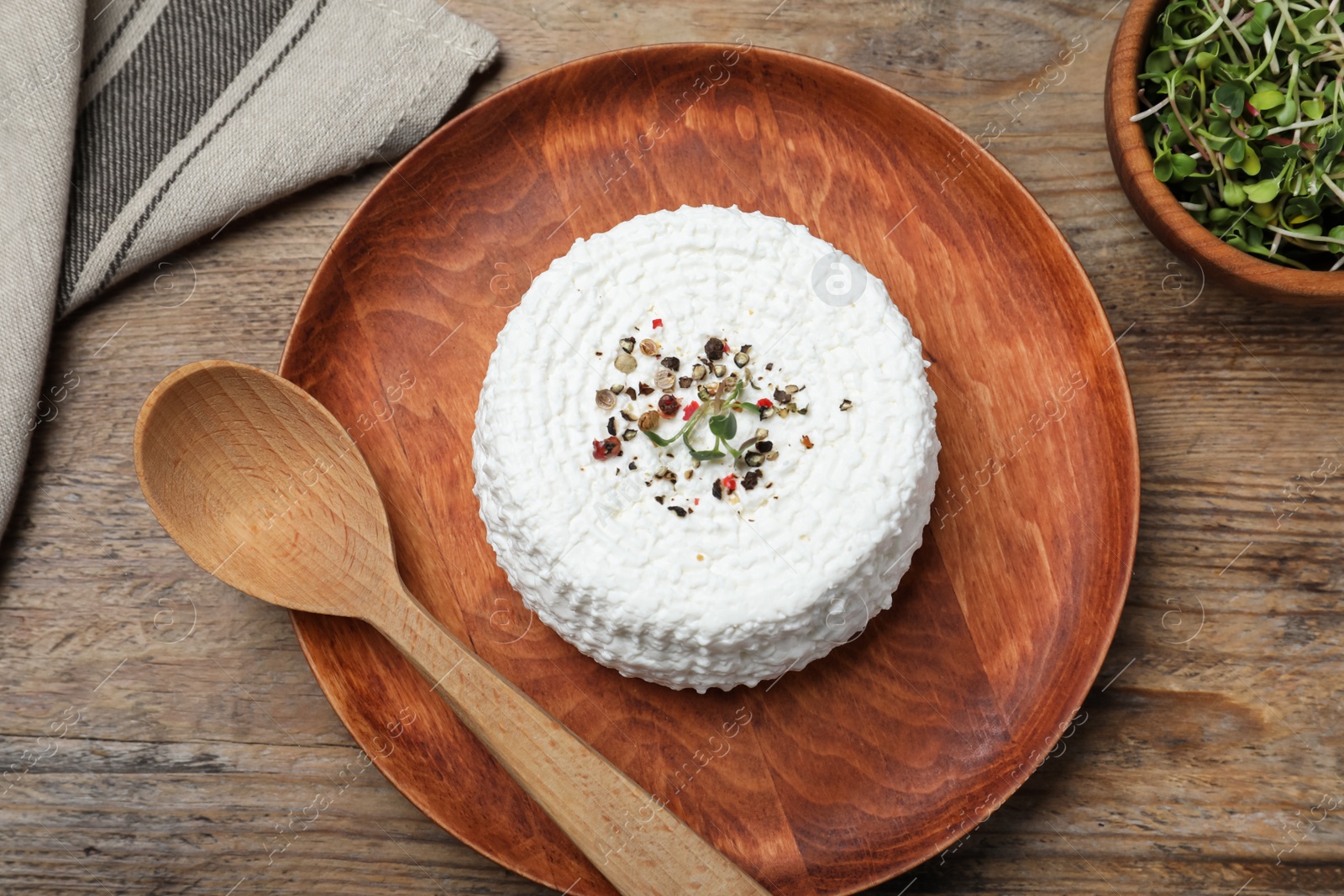 Photo of Plate of fresh cottage cheese with spice, microgreens and spoon on wooden table, flat lay