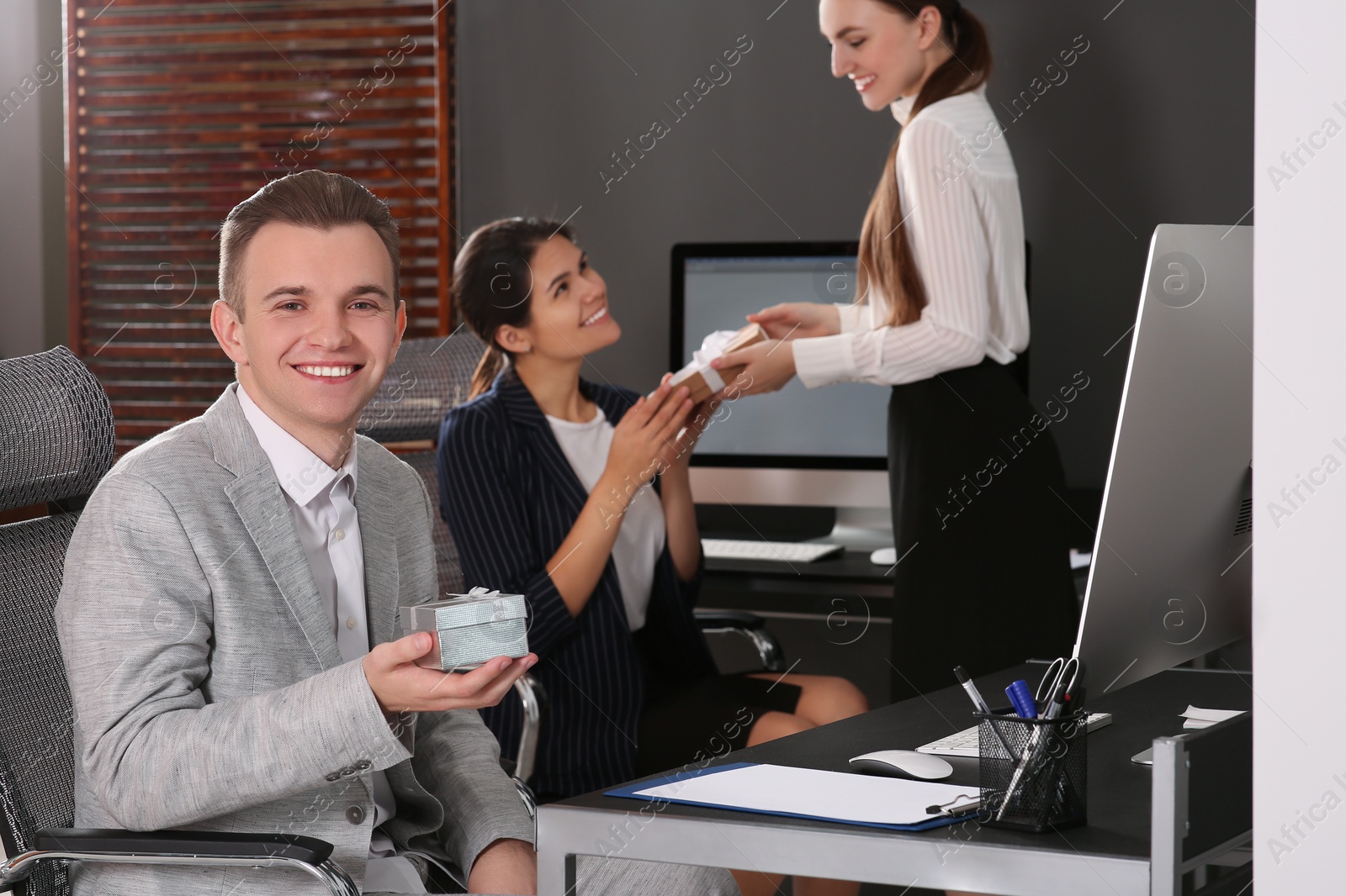 Photo of Happy man holding festive box and woman presenting gift to her colleague in office