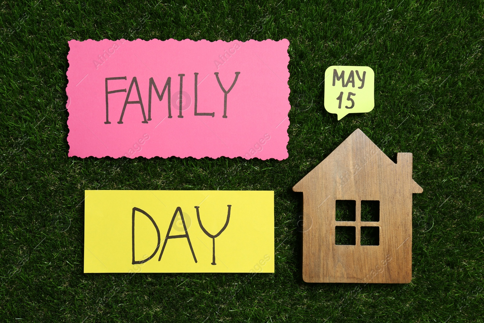 Photo of Cards with text Family Day and wooden house figure on green grass, flat lay