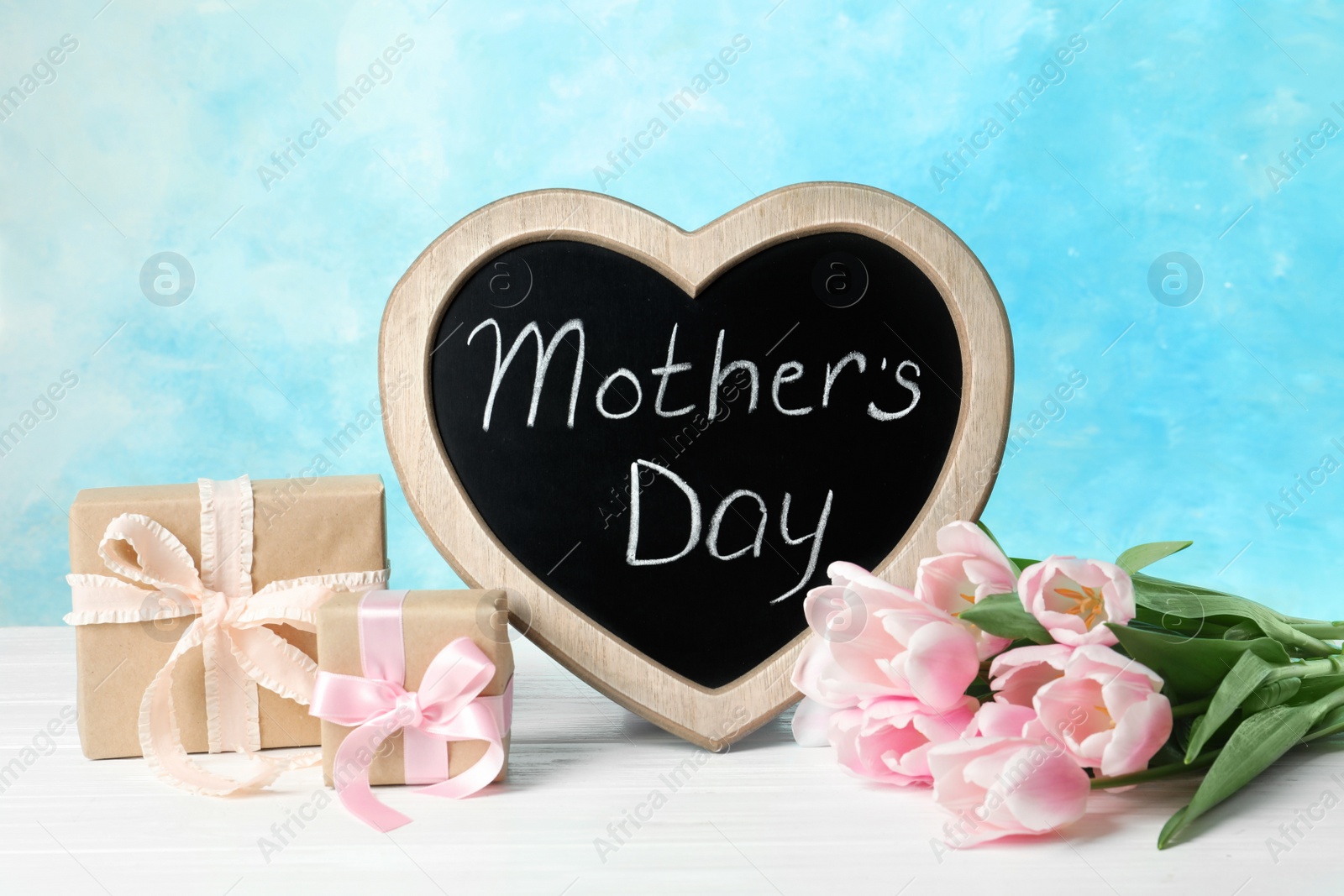 Photo of Chalkboard with text MOTHER'S DAY, tulips and gift boxes on table