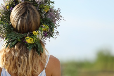 Photo of Young woman wearing wreath made of beautiful flowers outdoors on sunny day, back view