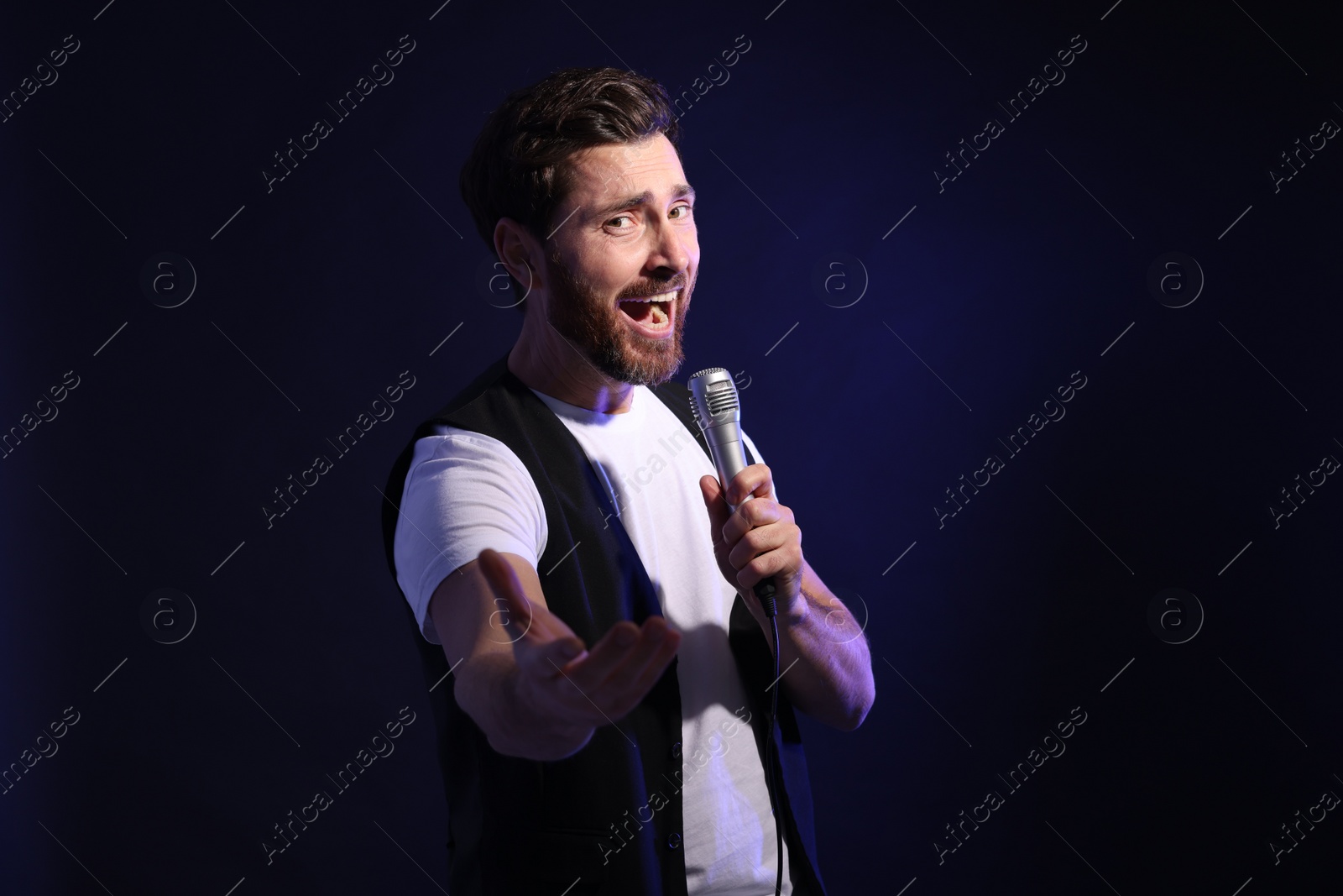 Photo of Handsome man with microphone singing on dark blue background