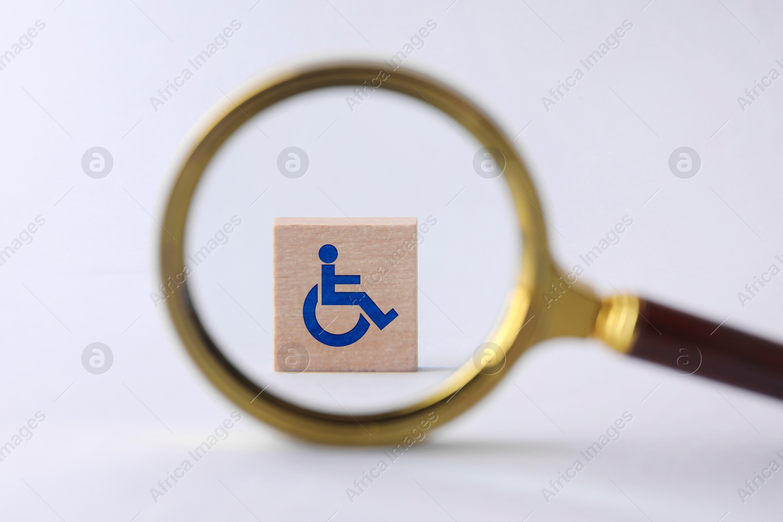 Image of Inclusion concept. Wooden cube with international symbol of access, view through magnifying glass