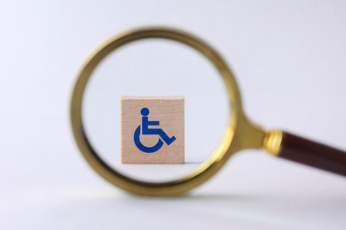 Inclusion concept. Wooden cube with international symbol of access, view through magnifying glass