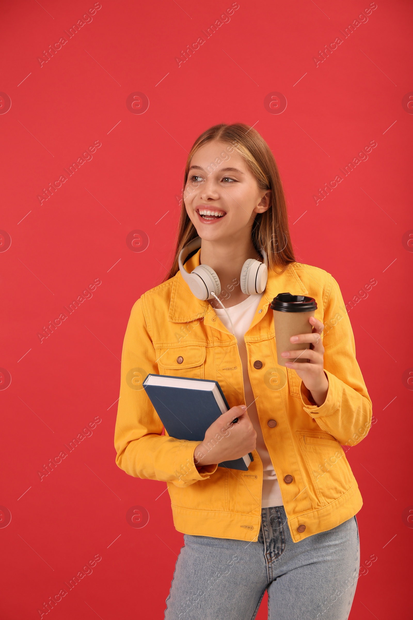 Photo of Teenage student with book, cup of coffee and headphones on red background