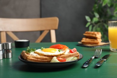 Photo of Delicious Belgian waffle with fried egg, salmon, cream cheese and vegetables served on green wooden table
