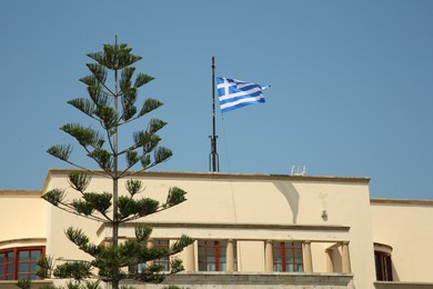 Picturesque view of beautiful building with flag of Greece and tree under blue sky