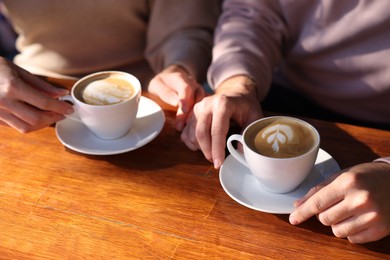 Photo of Couple with cups of aromatic coffee at wooden table in cafe, closeup