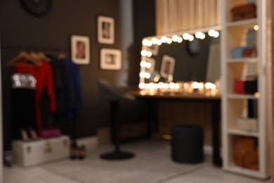 Blurred view of makeup room with stylish mirror on dressing table, chair and clothes rack
