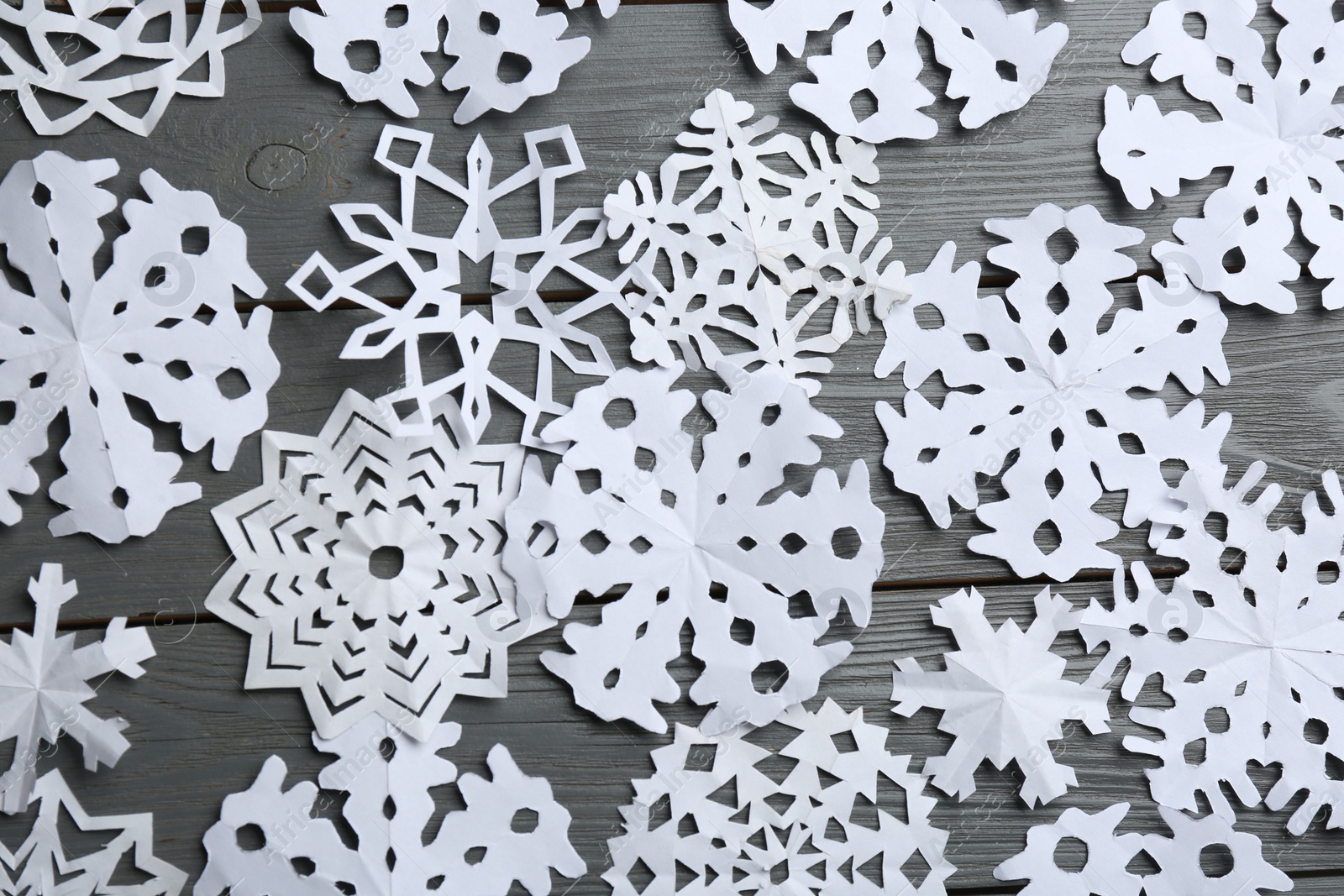 Photo of Many paper snowflakes on grey wooden background, flat lay