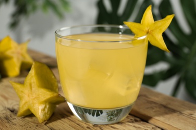 Photo of Delicious carambola juice in glass on wooden table, closeup