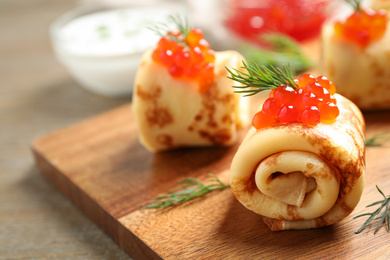 Delicious thin pancakes with red caviar on wooden board, closeup