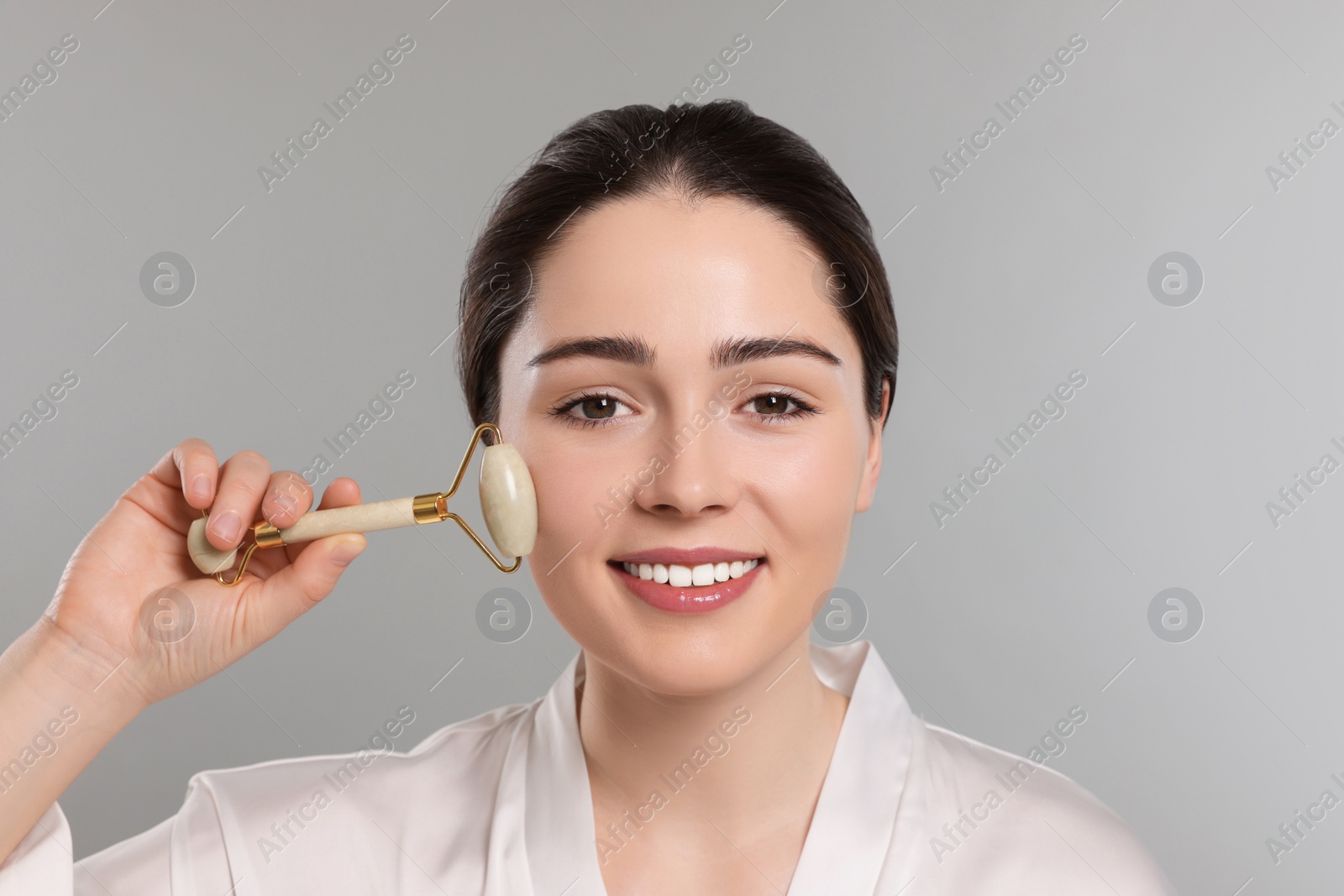 Photo of Young woman massaging her face with jade roller on grey background