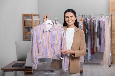 Dry-cleaning service. Happy woman holding hanger with shirt in plastic bag indoors