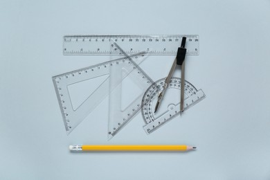 Photo of Different rulers with measuring length markings and compass on light grey background, flat lay