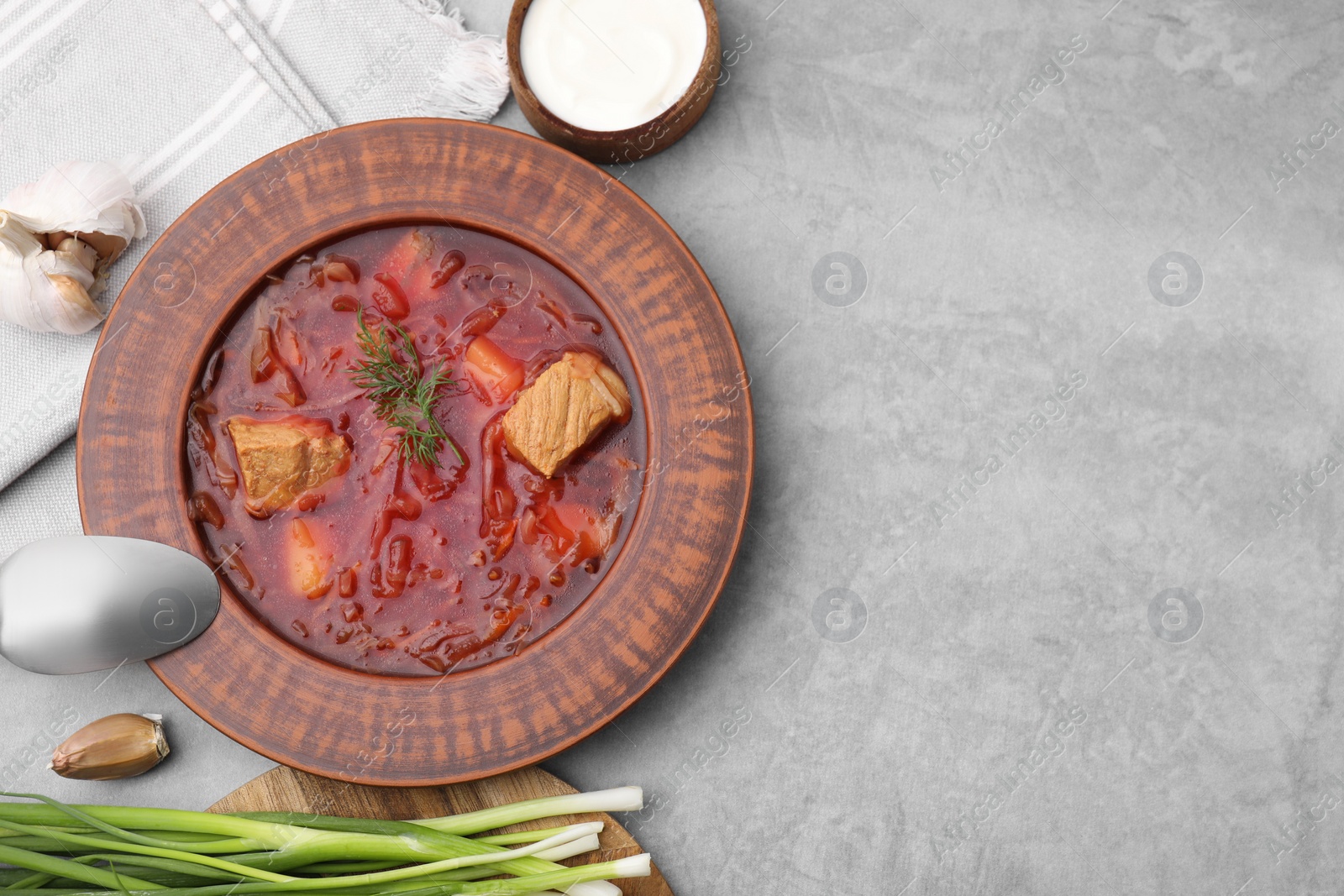 Photo of Bowl of delicious borscht, garlic, sour cream and onions on light grey table, flat lay. Space for text