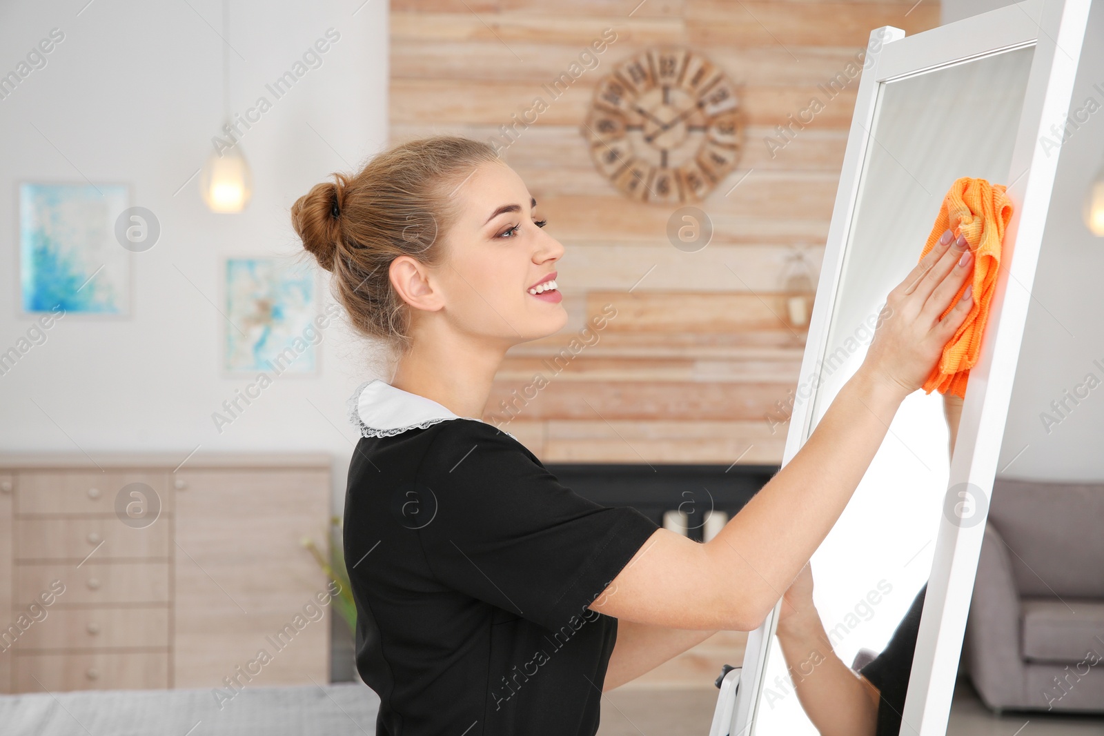 Photo of Young chambermaid wiping mirror with rag in hotel room