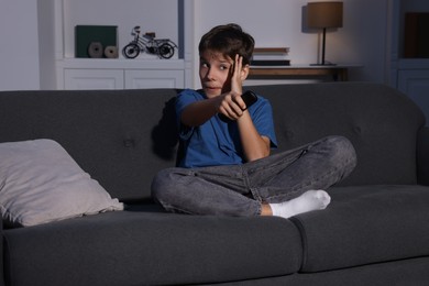 Emotional boy changing TV channels with remote control on sofa at home