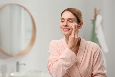 Photo of Beautiful woman removing makeup with cotton pad indoors, space for text