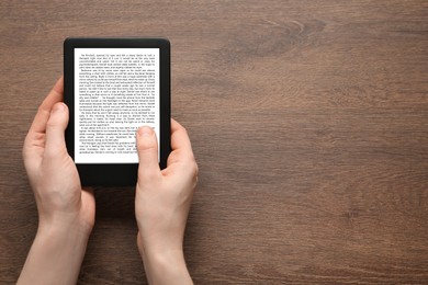 Image of Woman using e-book reader at wooden table, top view. Space for text