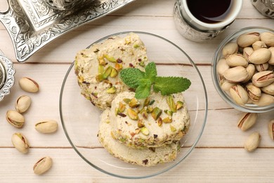 Photo of Tasty halva with pistachios and mint served on wooden table, flat lay