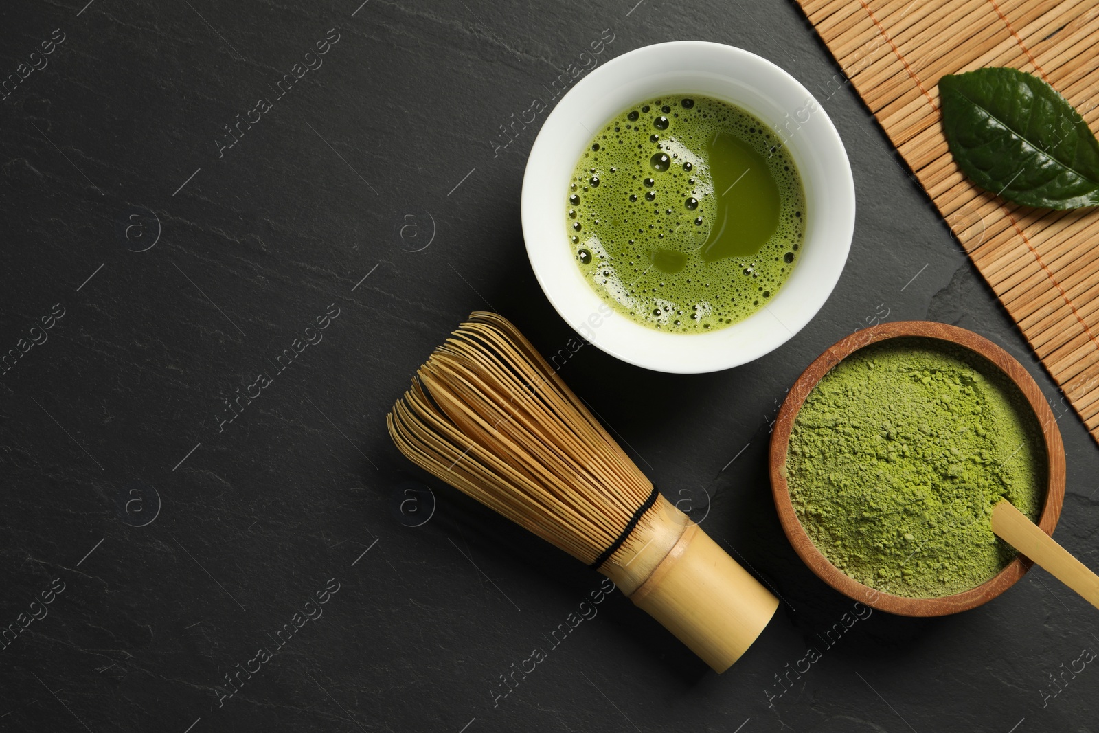 Photo of Cup of fresh matcha tea, green powder and bamboo whisk on black table, flat lay. Space for text