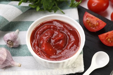 Photo of Organic ketchup in bowl, fresh tomatoes and garlic on table, closeup. Tomato sauce