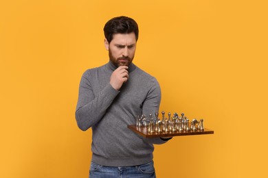 Photo of Thoughtful man holding chessboard with game pieces on yellow background