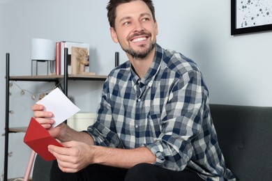 Happy man reading greeting card on sofa in living room