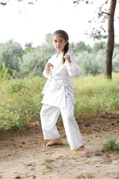 Photo of Cute little girl in kimono practicing karate outdoors