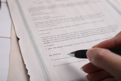 Woman signing last will and testament at table, closeup