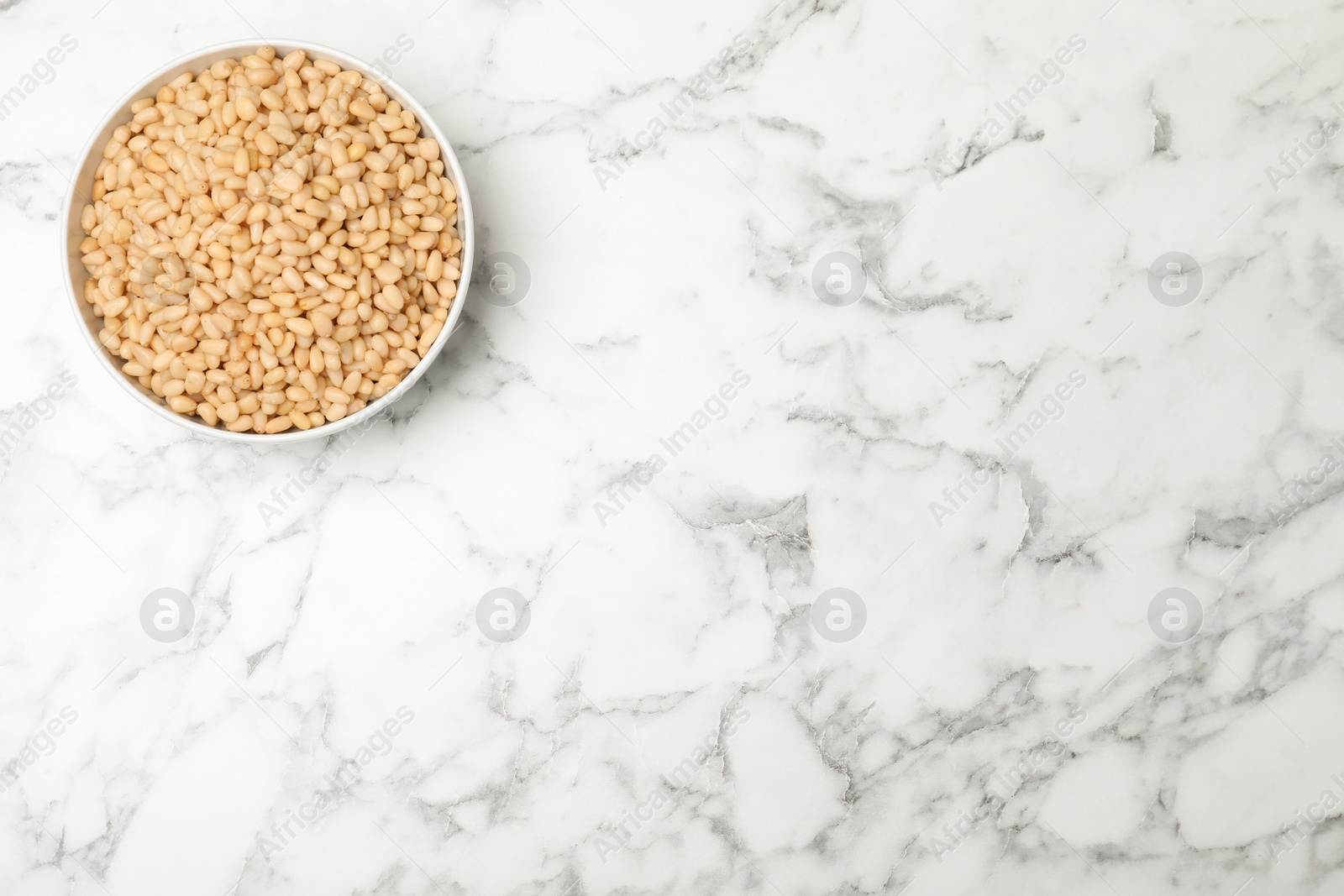 Photo of Bowl with pine nuts on marble background, top view. Space for text