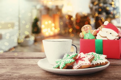 Image of Christmas cookies and cup of hot drink on wooden table in decorated room 