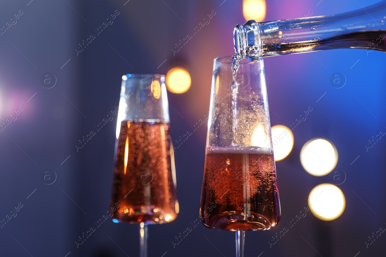Photo of Rose champagne pouring from bottle into glass on color background, closeup. Space for text