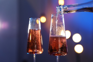 Photo of Rose champagne pouring from bottle into glass on color background, closeup. Space for text