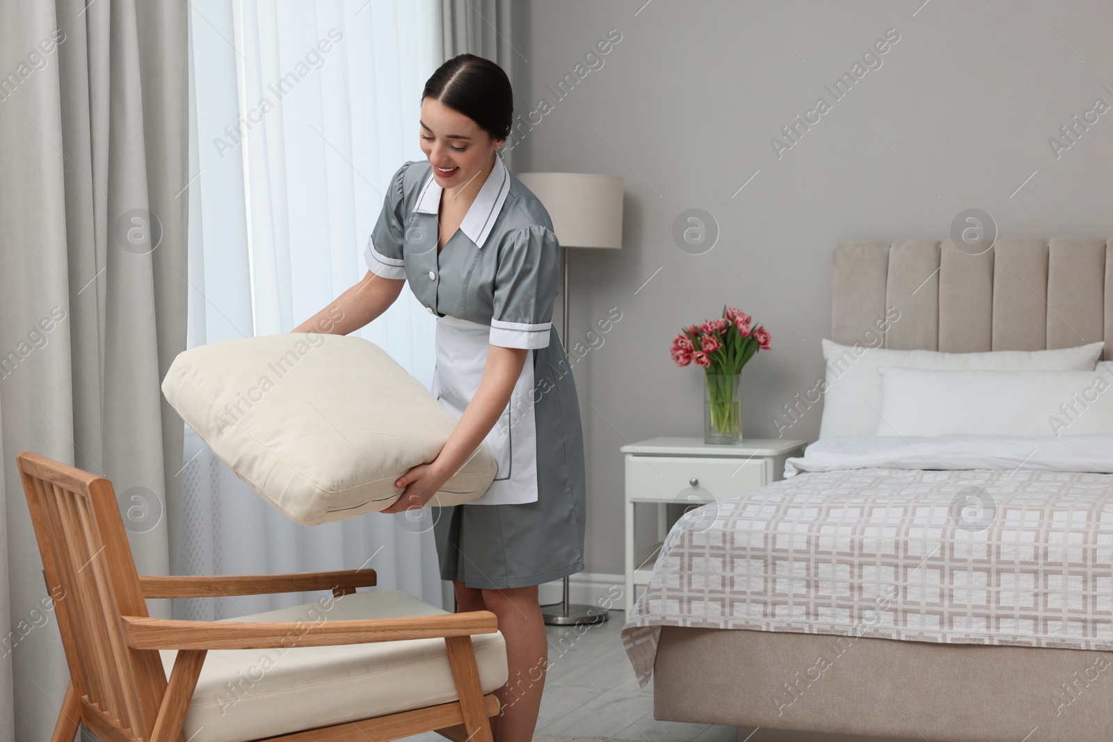Photo of Young chambermaid cleaning up bedroom in hotel