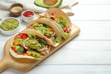 Delicious tacos with guacamole, meat and vegetables on white wooden table. Space for text