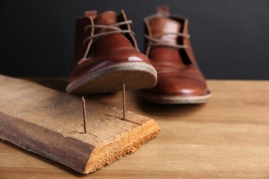 Photo of Metal nails in wooden plank and shoes on table