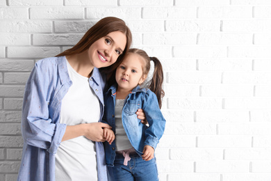 Young mother and little daughter near white brick wall. Space for text