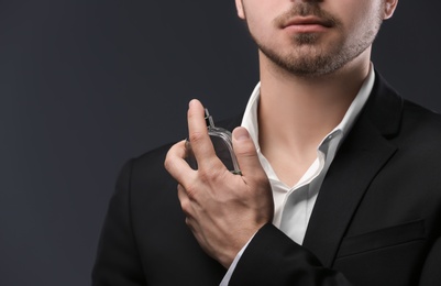 Photo of Handsome man in suit using perfume on dark background, closeup