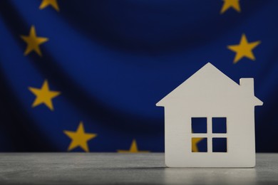 Photo of House model on light grey table against flag of European Union. Space for text