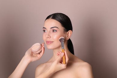 Photo of Professional makeup artist applying powder onto beautiful young woman's face with brush on dusty rose background