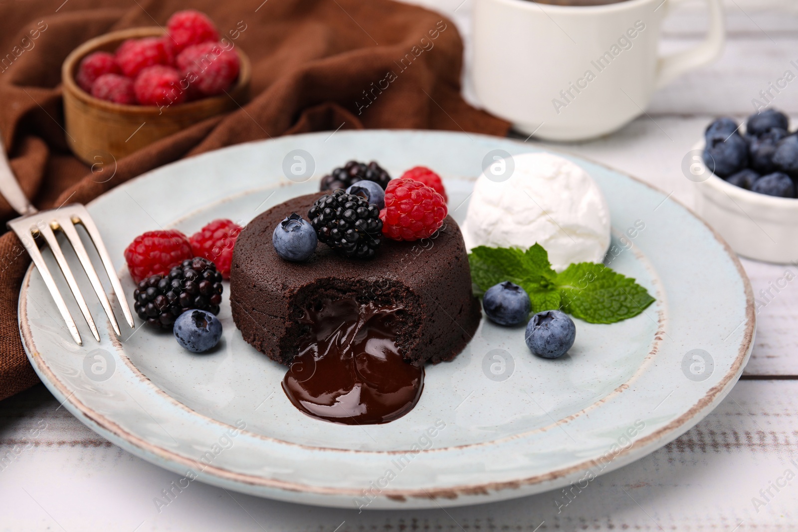 Photo of Delicious chocolate fondant served with fresh berries and ice cream on white wooden table, closeup
