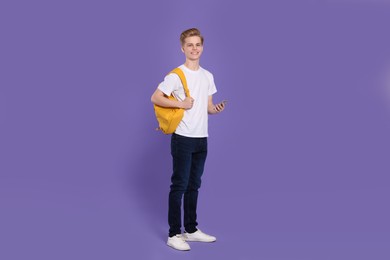 Photo of Teenage boy with backpack using smartphone on purple background