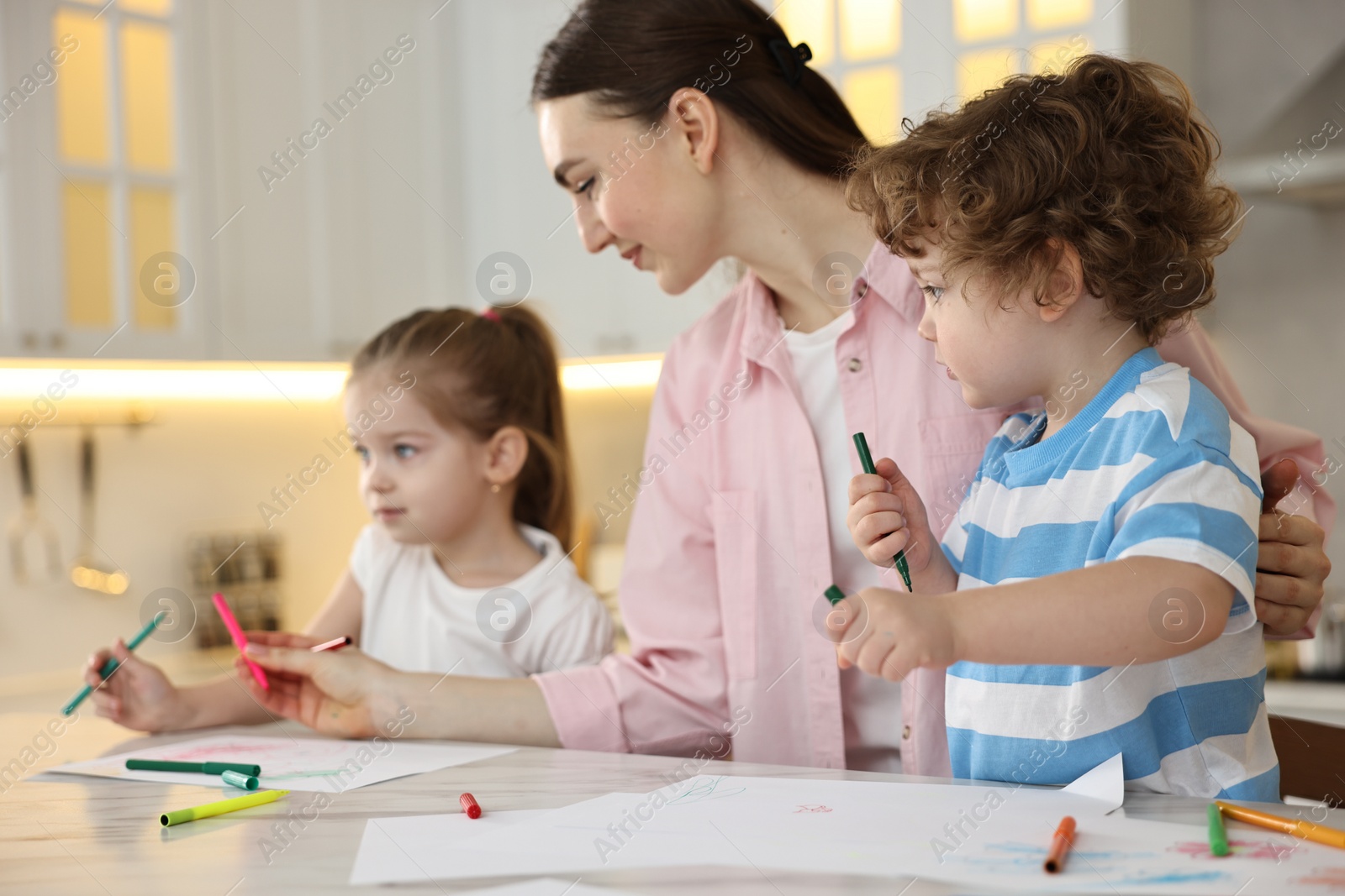 Photo of Mother and her little children drawing with colorful markers at table in kitchen