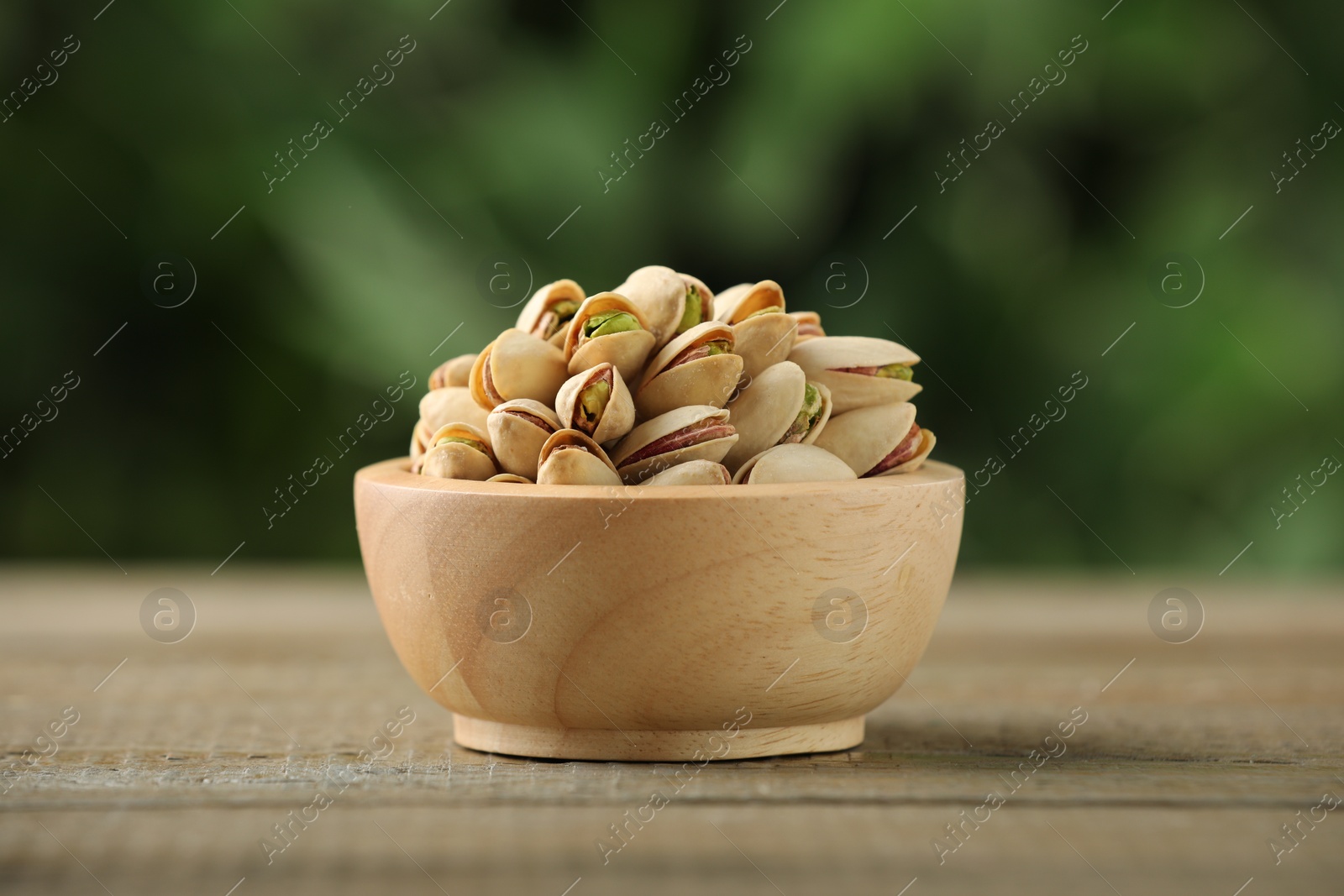 Photo of Tasty pistachios in bowl on wooden table against blurred background, closeup